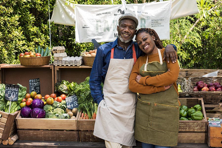 Business Insurance - a Couple Selling Produce at a Farmers Market Food Stand, Smiling and Wearing Work Aprons