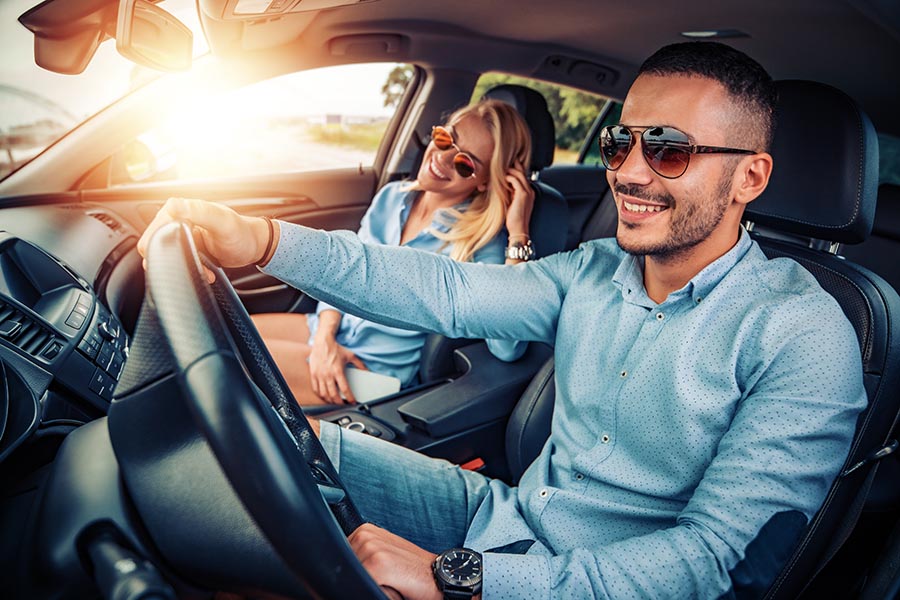 Personal Insurance - a Couple Driving in Their Car on a Sunny Day, Smiling and Wearing Blue Shirts and Sunglasses